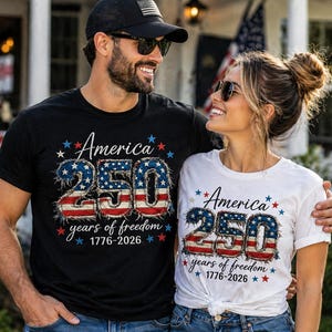 May include: Black and white t-shirts with the text "America 250 years of freedom 1776-2026" in red, white, and blue. The design features stars and the number 250 in a distressed American flag style.