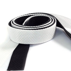 May include: A roll of black and white webbing, a type of strong fabric tape, is shown on a white background.
