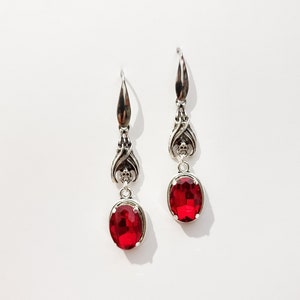 May include: A pair of silver dangle earrings with red oval-shaped gemstones.