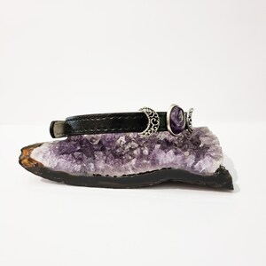 May include: A black leather bracelet with three silver crescent moon charms and a purple amethyst stone.