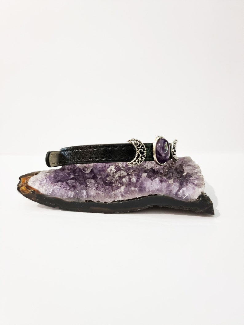 May include: A black leather bracelet with three silver crescent moon charms and a purple amethyst stone.