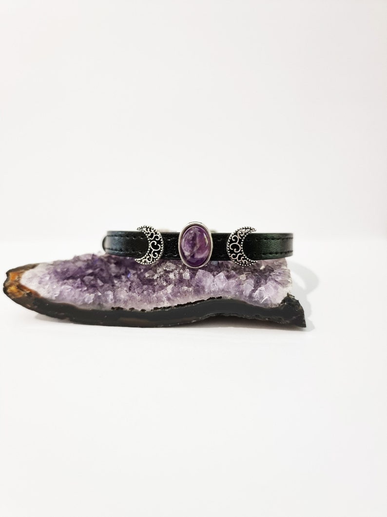 May include: A black leather bracelet with silver crescent moon charms and a purple amethyst stone in the center.
