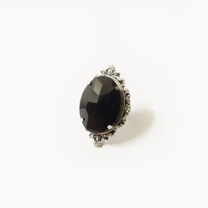 May include: A silver ring with a large, black, faceted gemstone set in an ornate, floral design.