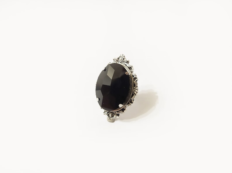 May include: A silver ring with a large, black, faceted gemstone set in an ornate, floral design.