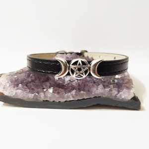 May include: A black leather choker necklace with a silver triple moon and pentagram charm. The necklace is resting on a purple amethyst crystal.