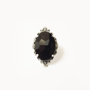 May include: A silver ring with a large, black, faceted gemstone set in an ornate, oval-shaped frame.