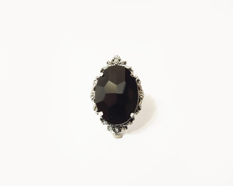 May include: A silver ring with a large, black, faceted gemstone set in an ornate, oval-shaped frame.
