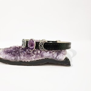 May include: A black leather bracelet with three silver crescent moon charms and a purple amethyst stone.