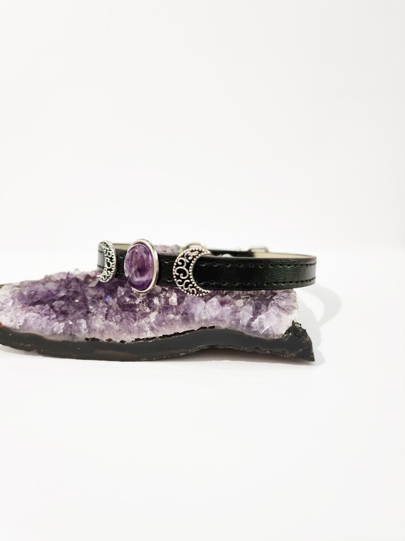 May include: A black leather bracelet with three silver crescent moon charms and a purple amethyst stone.