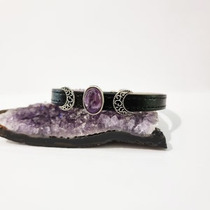 May include: A black leather bracelet with three silver crescent moon charms and a purple amethyst gemstone in the center.