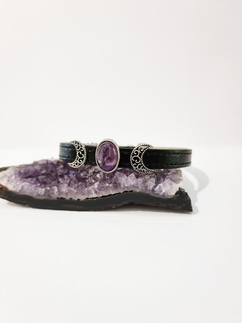 May include: A black leather bracelet with three silver crescent moon charms and a purple amethyst gemstone in the center.