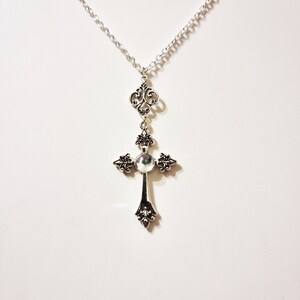 Pu&ograve; includere: Una collana con catena d'argento con un ciondolo a forma di croce d'argento con una pietra iridescente al centro. La croce presenta dettagli decorativi ed &egrave; attaccata a una delicata catena d'argento.