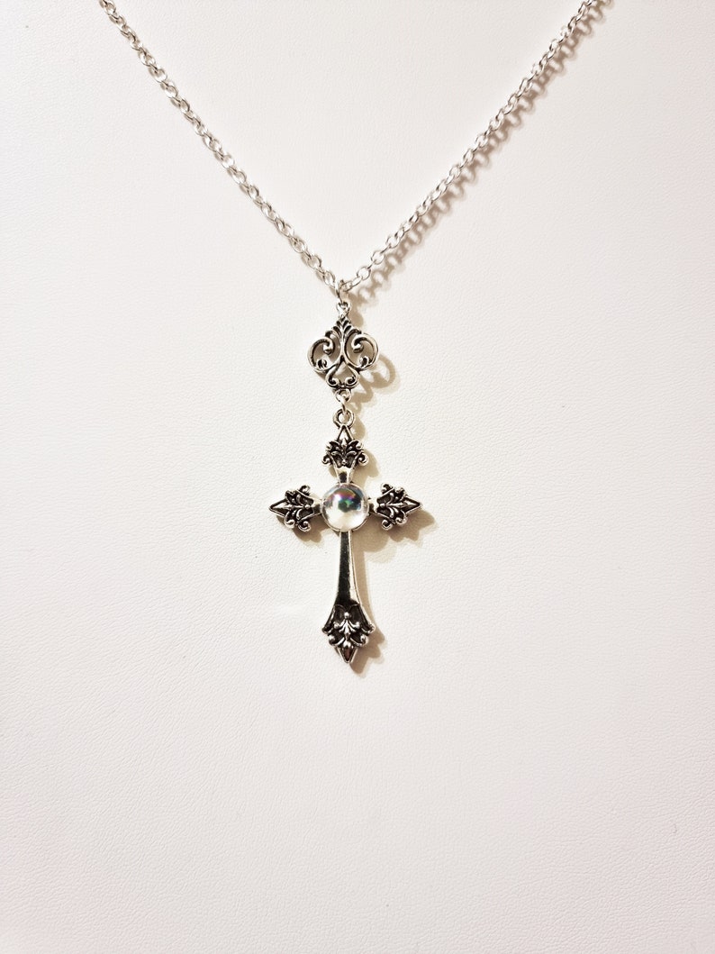 Pu&ograve; includere: Una collana con catena d'argento con un ciondolo a forma di croce d'argento con una pietra iridescente al centro. La croce presenta dettagli decorativi ed &egrave; attaccata a una delicata catena d'argento.