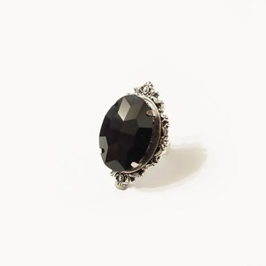 May include: A silver ring with a large, faceted black gemstone set in a decorative, ornate frame.