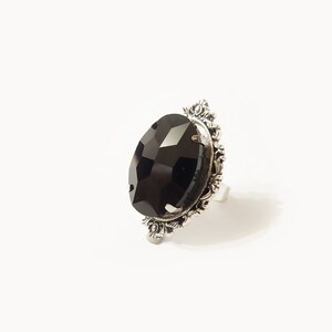 May include: A silver ring with a large, black, faceted gemstone set in a decorative, ornate frame.