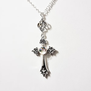 Pu&ograve; includere: Una collana con catena d'argento con un ciondolo a forma di croce d'argento con un centro in vetro iridescente.