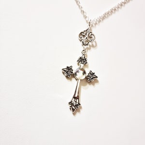Pu&ograve; includere: Collana con catena d'argento con un ciondolo a forma di croce d'argento con una pietra iridescente al centro.