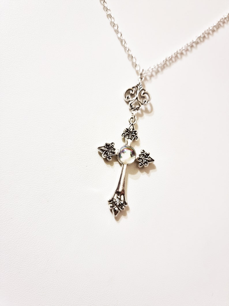 Pu&ograve; includere: Collana con catena d'argento con un ciondolo a forma di croce d'argento con una pietra iridescente al centro.