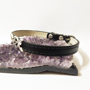 May include: Black leather pet collar with a silver triple moon and pentagram charm. The collar is resting on a bed of amethyst crystals.