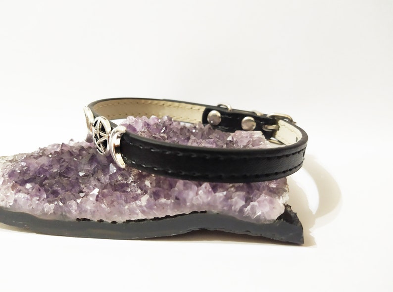 May include: Black leather pet collar with a silver triple moon and pentagram charm. The collar is resting on a bed of amethyst crystals.
