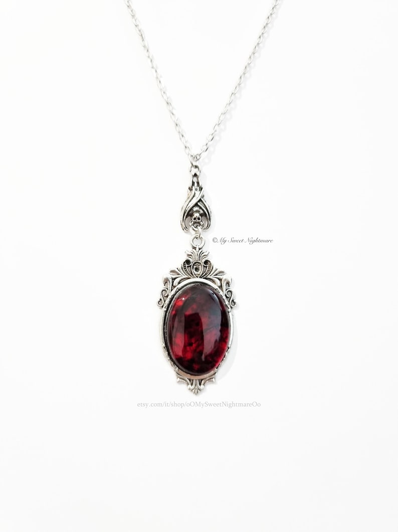 May include: Silver-toned pendant necklace featuring an oval, deep red gemstone. The pendant has an ornate, gothic-style frame with skull accents. The necklace is suspended from a delicate chain. The text "&copy; My Sweet Nightmare" is visible.