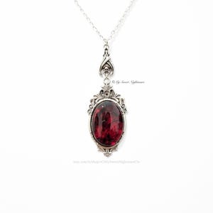 May include: Silver-toned pendant necklace with a large, oval, deep red stone. The pendant has an ornate, gothic-style frame and a delicate chain. The design includes skull accents. The Etsy shop name "oMySweetNightmareOo" is visible.