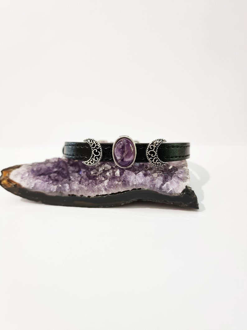 May include: A black leather bracelet with three silver crescent moon charms and a purple amethyst stone in the center.