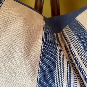 Puede incluir: Primer plano de una almohada a rayas con rayas beige y azul marino alternadas. La tela tiene un aspecto tejido texturizado.