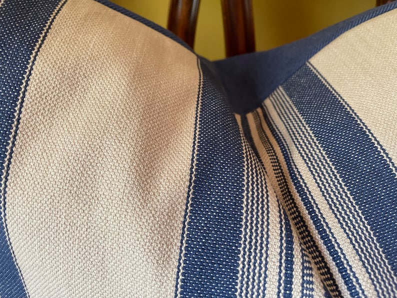 Puede incluir: Primer plano de una almohada a rayas con rayas beige y azul marino alternadas. La tela tiene un aspecto tejido texturizado.