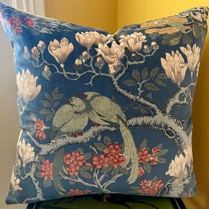 May include: A blue throw pillow with a floral pattern featuring pink flowers, green leaves, and two birds. The birds are perched on a branch and have long tails.