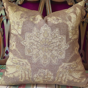 May include: A brown and gold throw pillow with a floral pattern. The pillow is made of a textured fabric and has a subtle sheen.