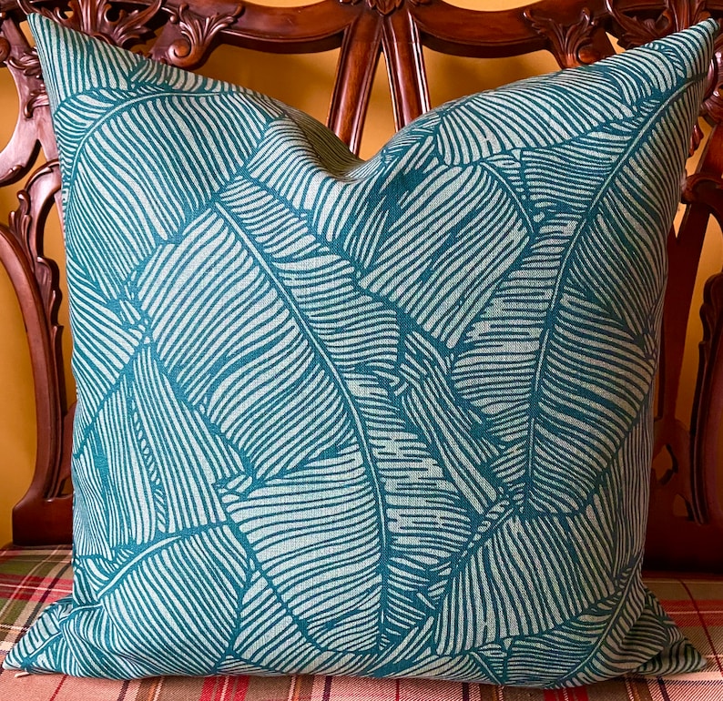May include: Teal blue throw pillow with a white banana leaf pattern.
