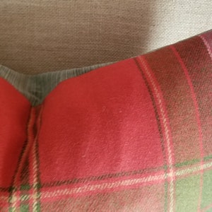 Puede incluir: Coj&iacute;n de tiro de cuadros rojos, verdes y marrones con una textura suave y peluda. El coj&iacute;n est&aacute; sentado en una silla de tela marr&oacute;n claro.