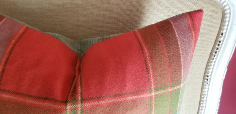 Puede incluir: Coj&iacute;n de tiro de cuadros rojos, verdes y marrones con una textura suave y peluda. El coj&iacute;n est&aacute; sentado en una silla de tela marr&oacute;n claro.