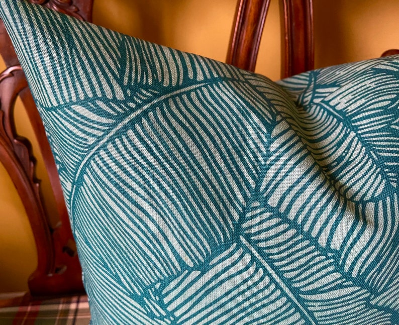 May include: A teal blue throw pillow with a white leaf pattern. The pillow is made of a textured fabric and has a subtle sheen.