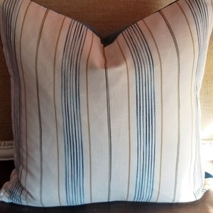 May include: A striped throw pillow with a light pink background and blue and tan stripes. The pillow has a blue border.