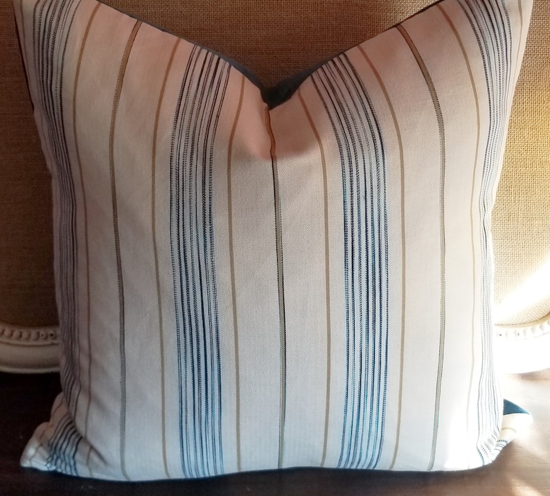 May include: A striped throw pillow with a light pink background and blue and tan stripes. The pillow has a blue border.