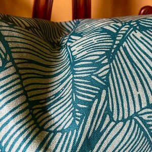 May include: Teal green throw pillow with a white leaf pattern. The pillow is made of a textured fabric.