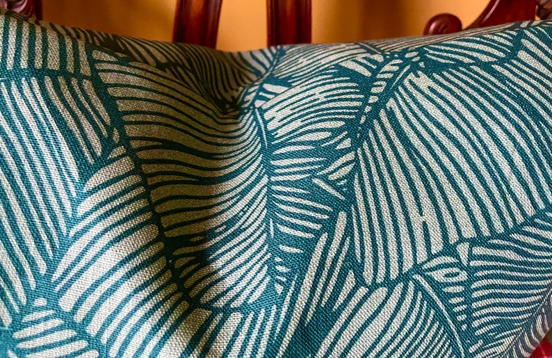 May include: Teal green throw pillow with a white leaf pattern. The pillow is made of a textured fabric.