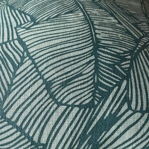 May include: Close-up of a teal fabric with a white leaf pattern. The fabric has a textured, woven look.