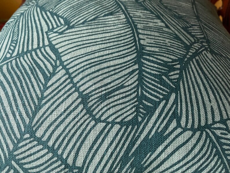 May include: Close-up of a teal fabric with a white leaf pattern. The fabric has a textured, woven look.