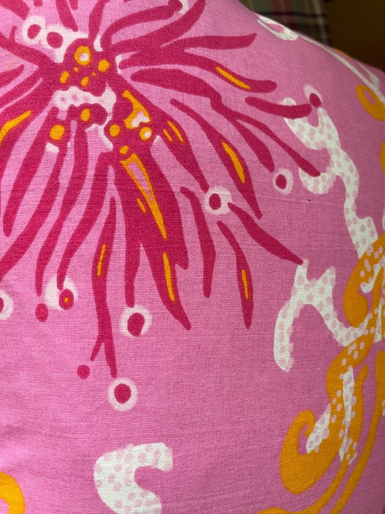 May include: Pink fabric with a floral pattern in shades of pink, yellow, and white. The pattern features a large flower with a central circle and radiating petals.