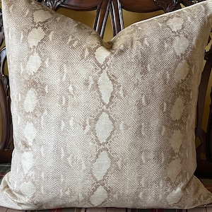 May include: A beige and brown patterned throw pillow with a snakeskin design. The pillow is sitting on a plaid chair.