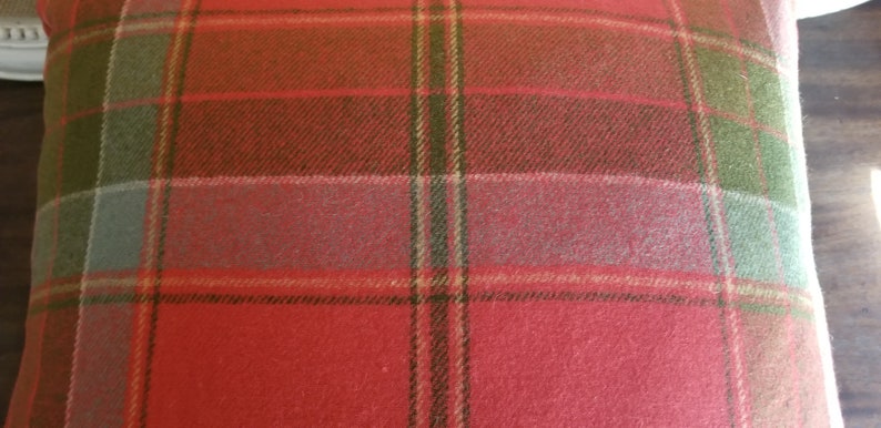Puede incluir: Coj&iacute;n de tiro de color rojo, verde y beige a cuadros con una textura suave y peluda.