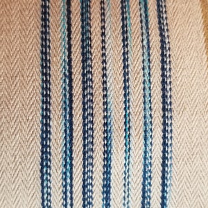 May include: Close-up of a beige fabric with vertical stripes in shades of blue and gold.
