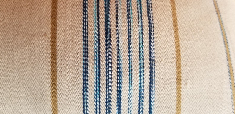 May include: Close-up of a beige fabric with vertical stripes in shades of blue and gold.