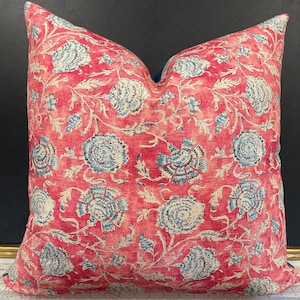 May include: Square decorative pillow with a vibrant red background and a repeating floral pattern in shades of blue and off-white. The pillow has a soft, textured appearance, suitable for adding a pop of color and pattern to any room.