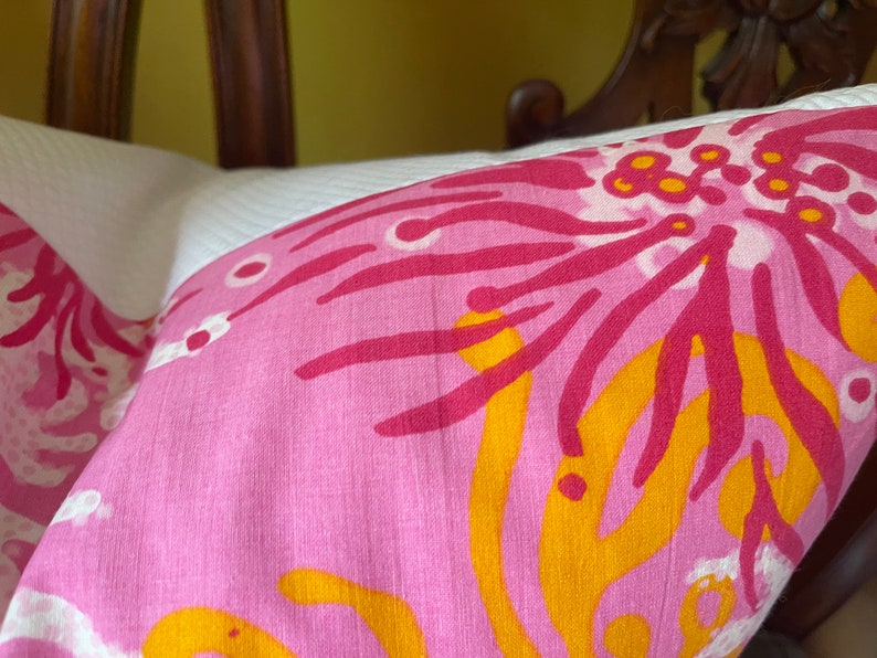 May include: Pink and white pillow with a floral pattern in shades of pink, yellow, and white. The pattern features large, stylized flowers with a bold, graphic design.