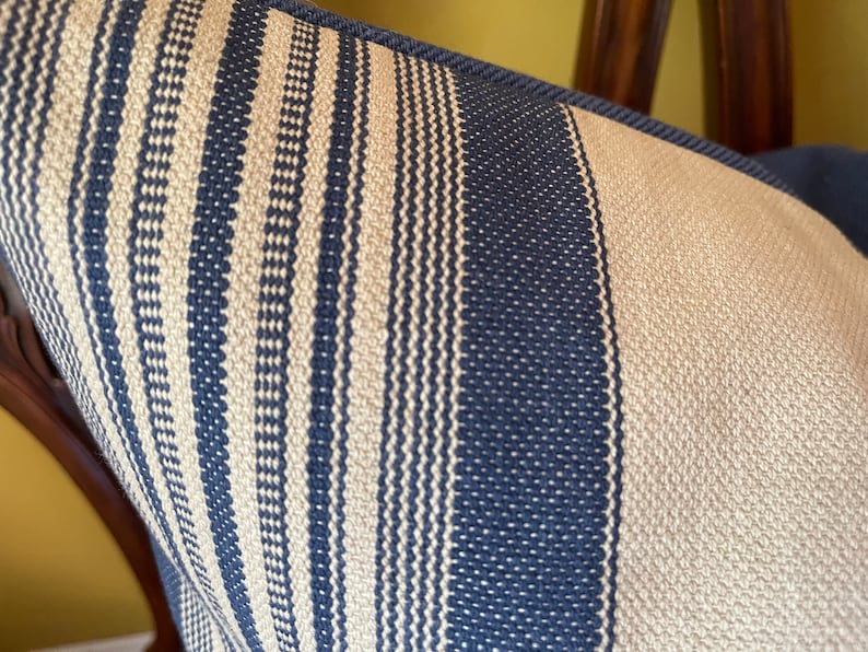 Puede incluir: Primer plano de una funda de coj&iacute;n a rayas azules y blancas. La tela tiene una textura tejida con peque&ntilde;os puntos blancos.