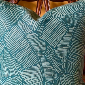 May include: A teal green throw pillow with a white leaf pattern. The leaves are stylized and resemble banana leaves.